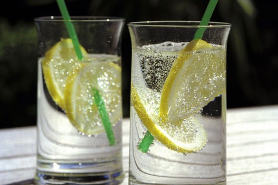 Two glasses with mineral water, lemon slices and straws standing in the sun.